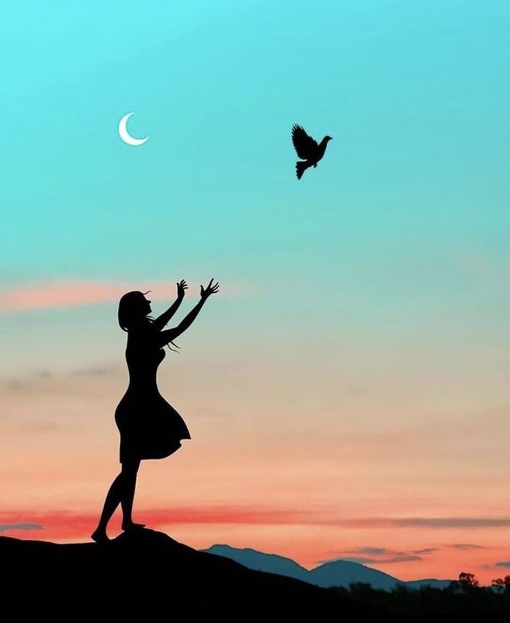 a woman reaching up to a bird in the air at sunset with mountains in the background