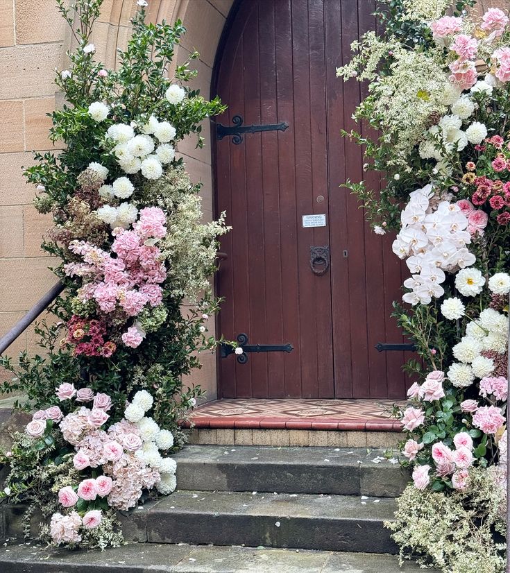 an entrance to a church with flowers growing on the steps and in front of it is a wooden door