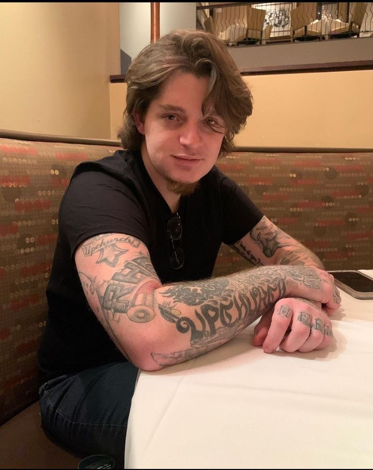 a man sitting at a table with his arms crossed and tattoos on his arm, looking to the side