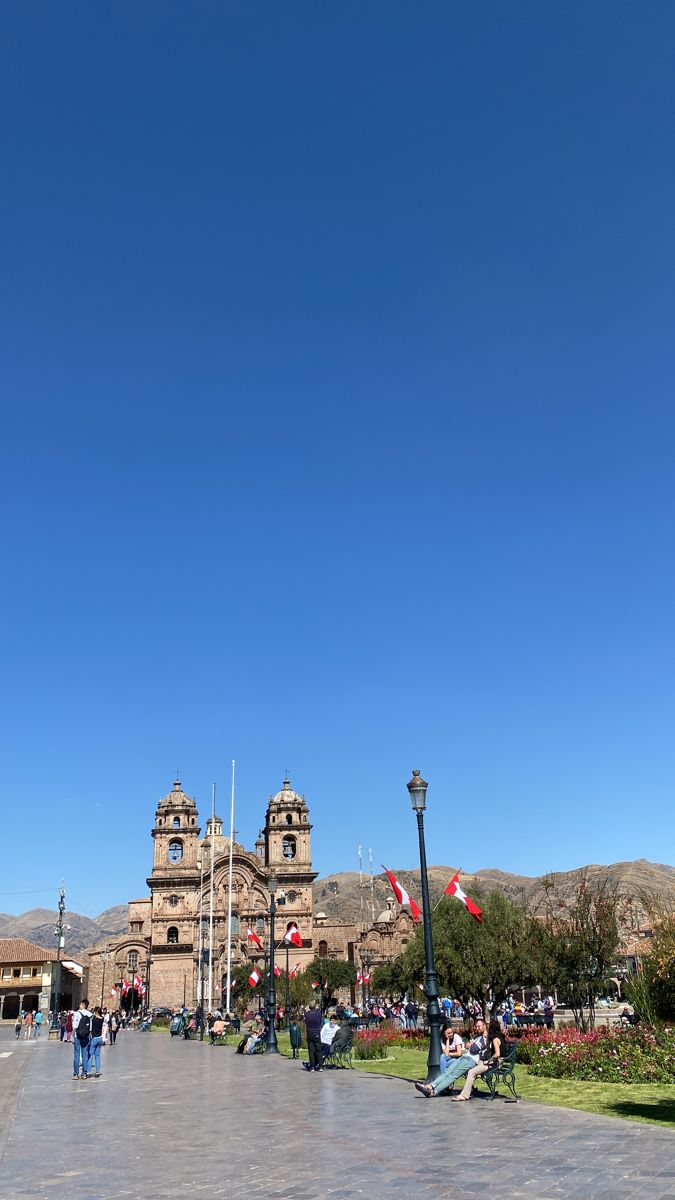 people are sitting on benches in front of a large building with tall towers and flags