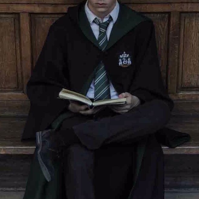 a man sitting on a bench with a book in his lap and wearing a green tie