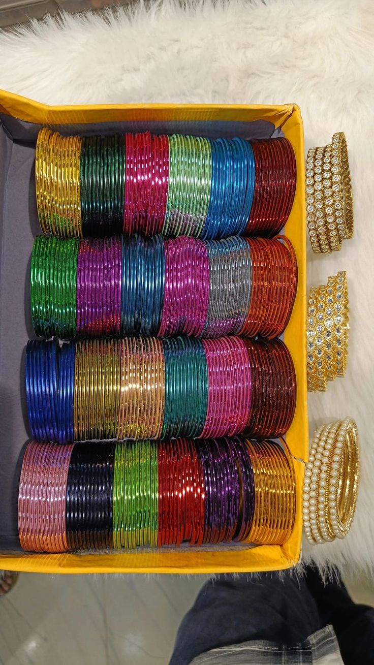 a yellow box filled with lots of different colored bracelets and bangles on top of a white furnishing