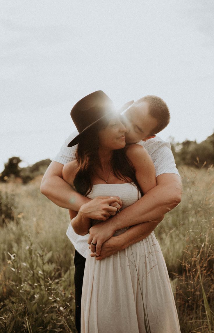 a man and woman embracing in the middle of a field with tall grass on either side