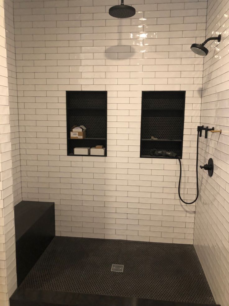 a white tiled shower with black flooring and shelves on the wall next to it