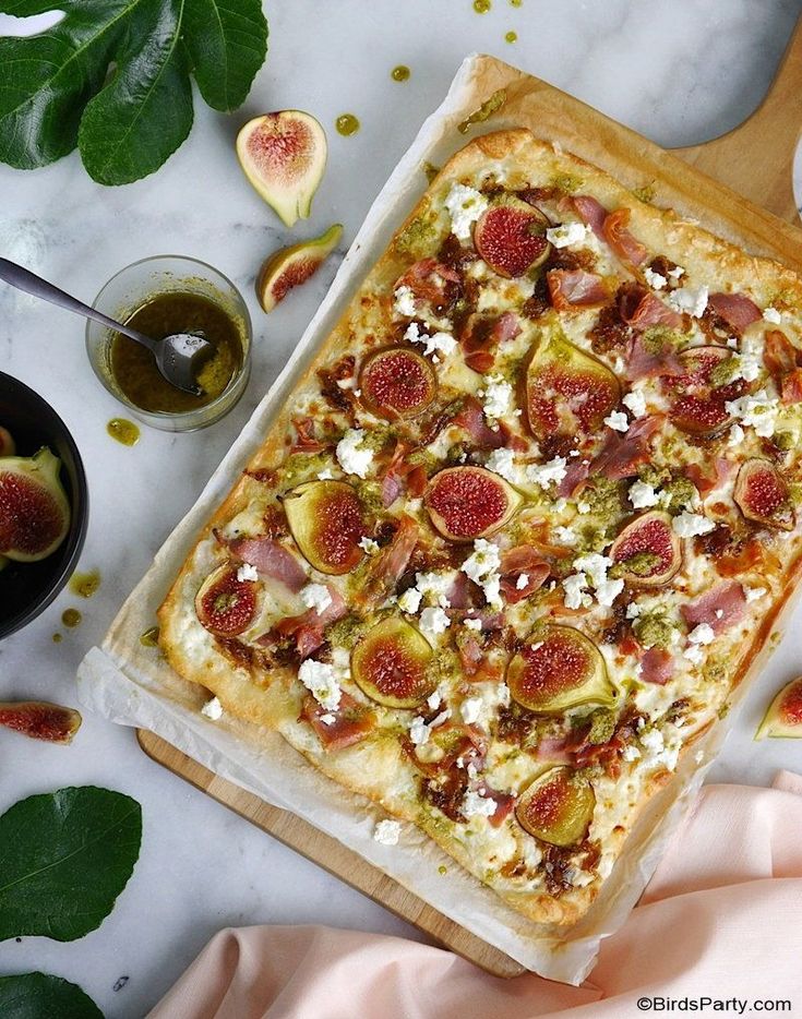 a pizza on a cutting board with figs and other food items around the table