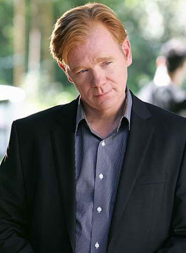 a man in a black suit and blue shirt is looking at something with his hand on his hip