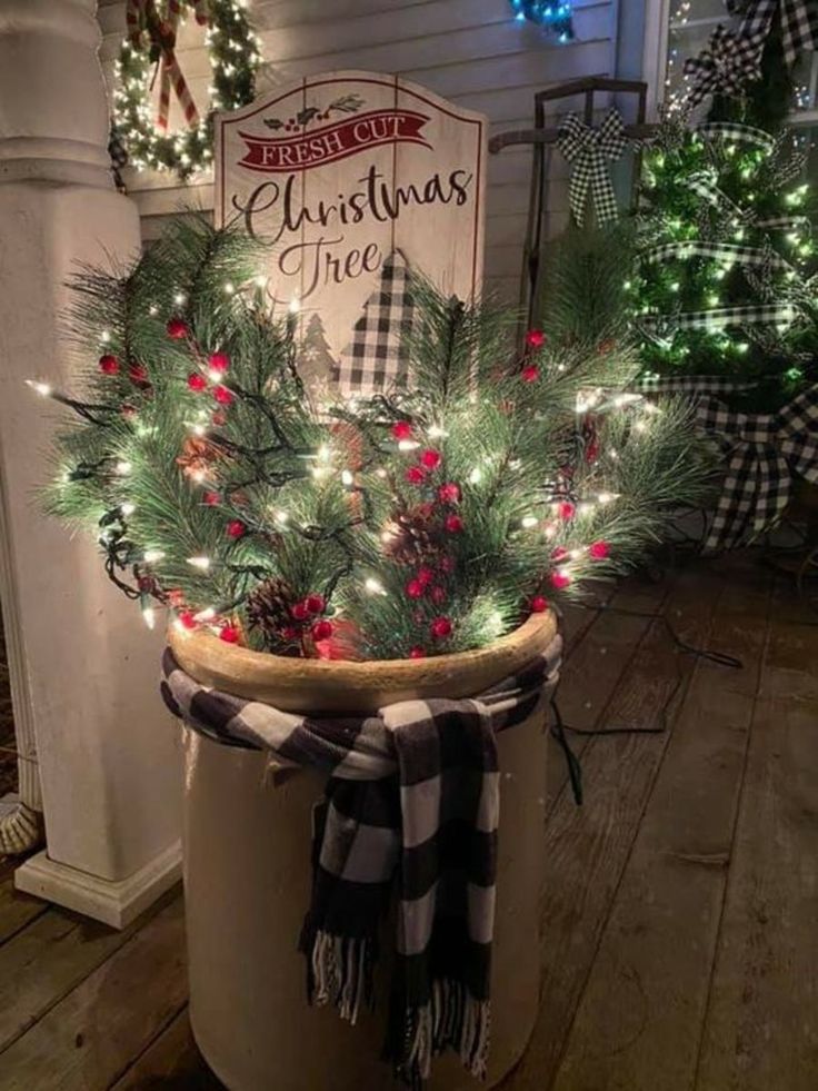 a christmas tree in a pot with lights on the top and a sign above it