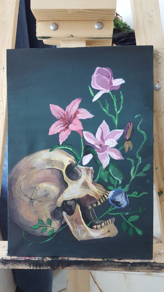 a painting of a skull and flowers on a black background with wooden easel in the foreground