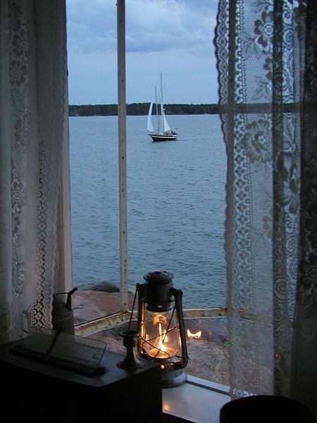 a lantern is lit on the window sill in front of an ocean view with a sailboat