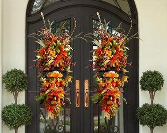 two large wreaths on the front door of a house with potted trees and bushes