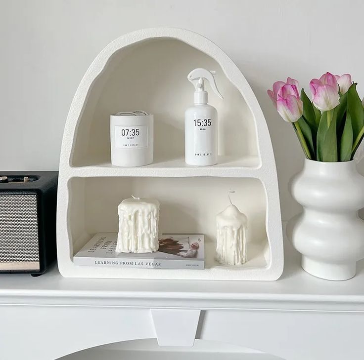 a white shelf with flowers and candles on it