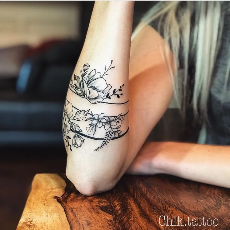 a woman with a tattoo on her arm sitting at a table and looking off into the distance