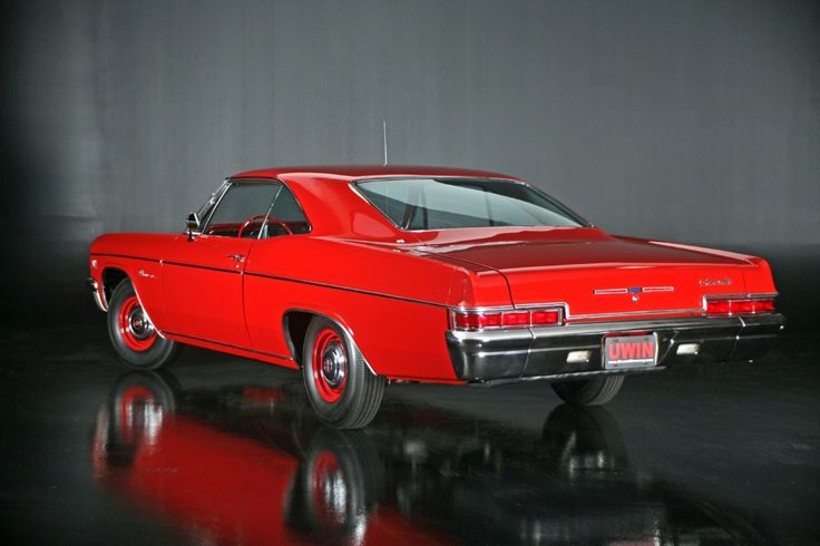 an old red car is parked in a dark room with reflections on the floor and walls