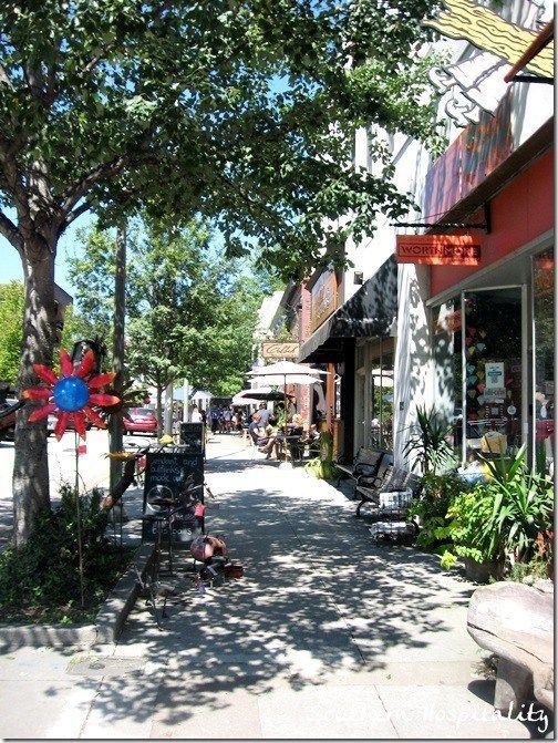 the sidewalk is lined with shops and trees