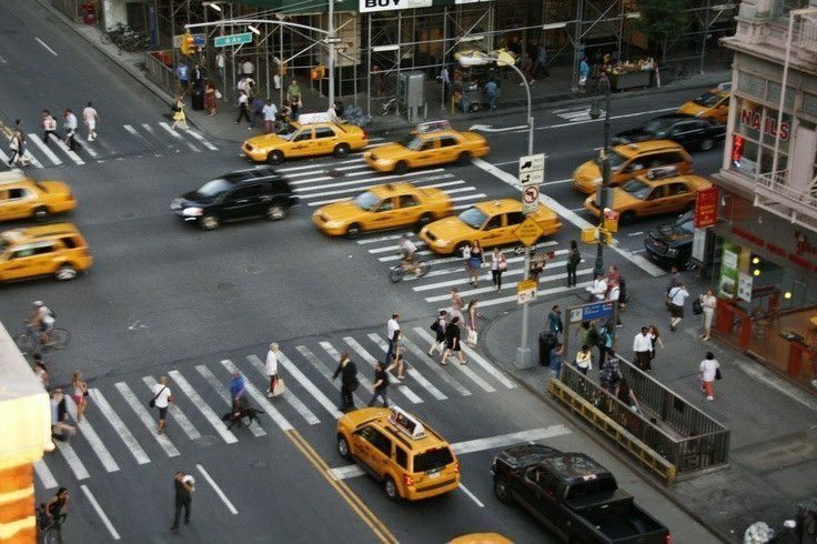 a busy city street filled with lots of yellow cabs and people crossing the street