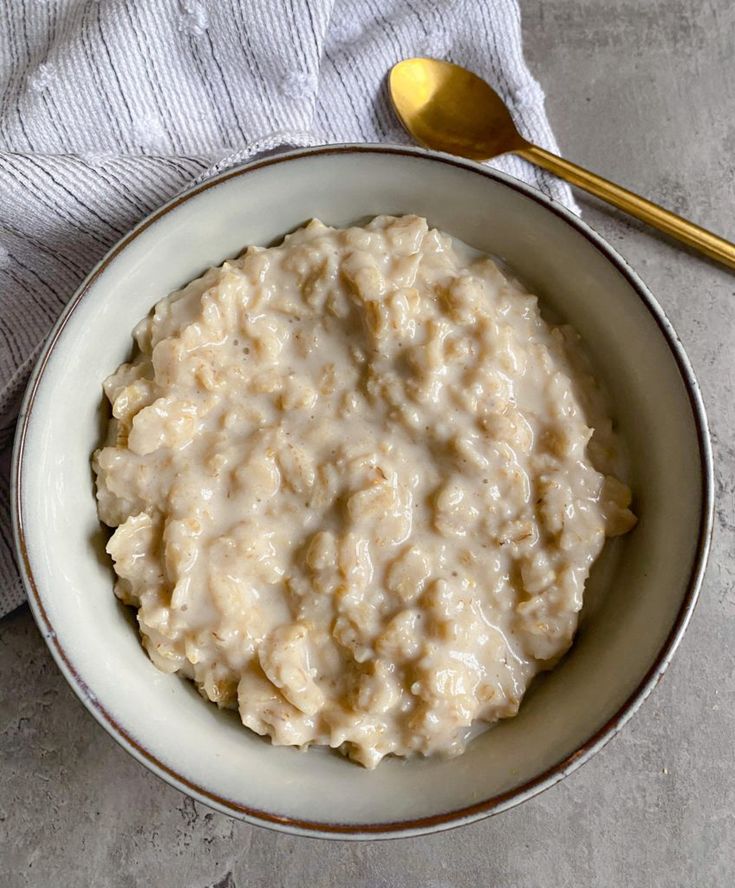 a white bowl filled with oatmeal next to a gold spoon and napkin