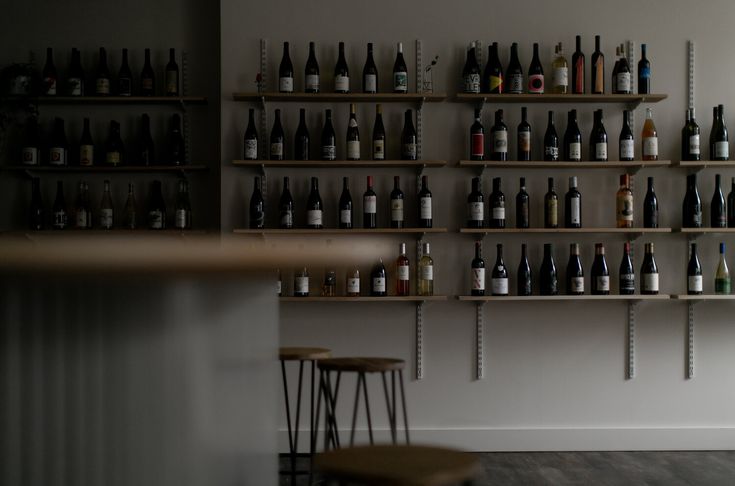 there are many bottles on the shelves in this room, and one is sitting next to two stools