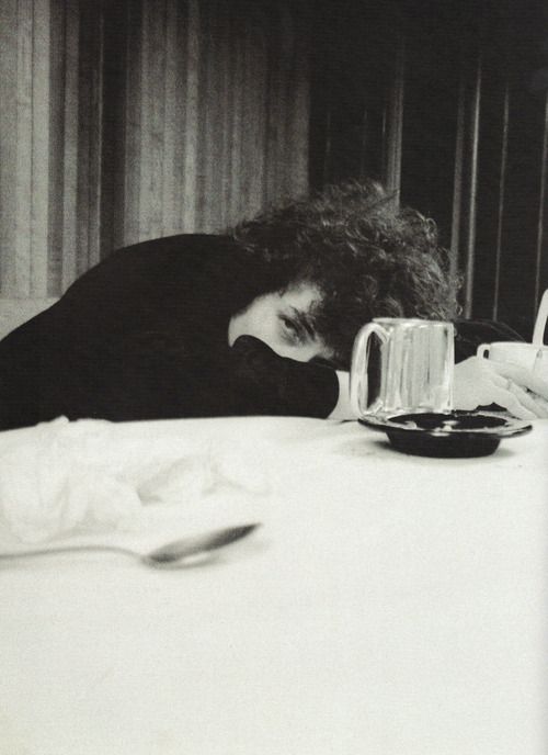 a black and white photo of a person sleeping on a bed with their head down