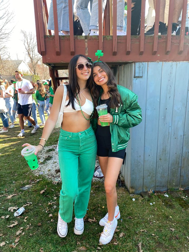 two young women standing next to each other in front of a wooden structure with people