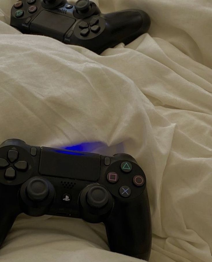 two video game controllers laying on top of a white bed sheet covered in sheets and pillows