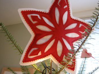 a red and white star ornament sitting on top of a christmas tree branch