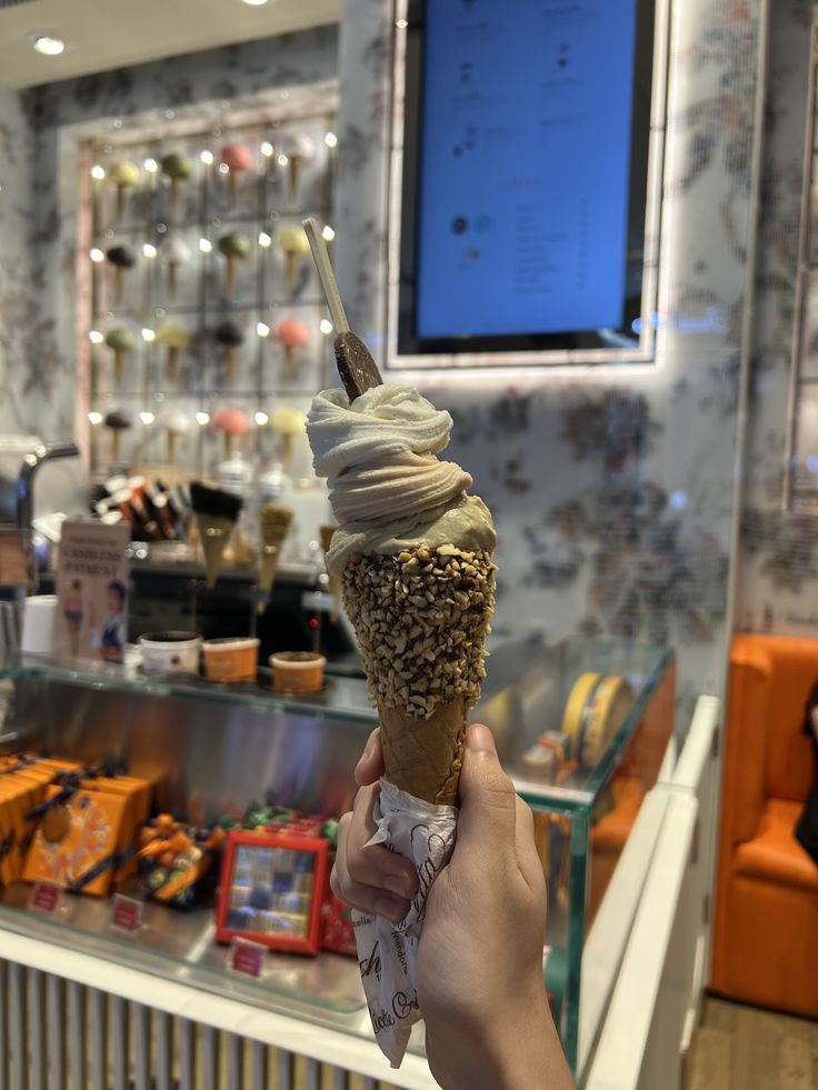 a person holding up an ice cream cone with sprinkles in front of a store