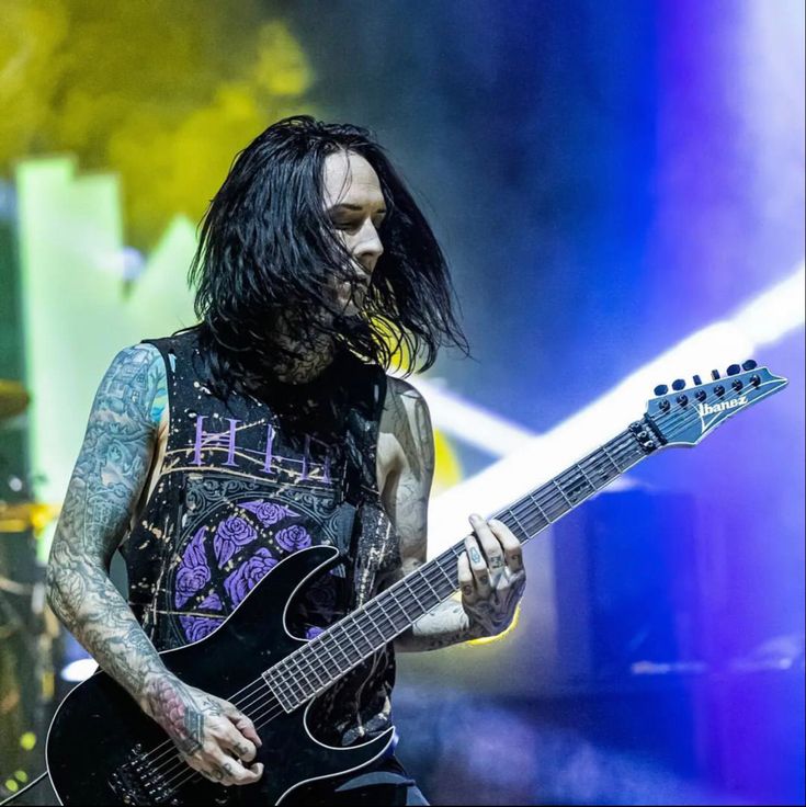 a man with long black hair playing a guitar at a music festival in front of blue and purple lights