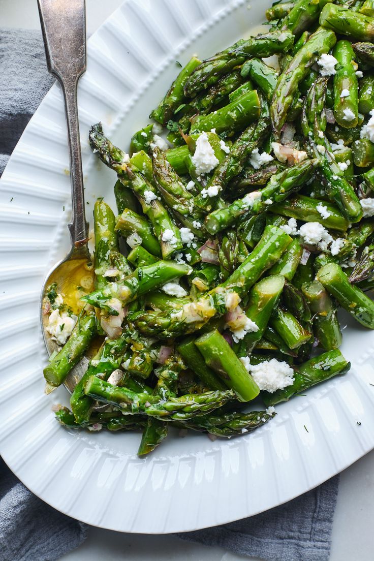 a white plate topped with asparagus covered in feta cheese next to a fork