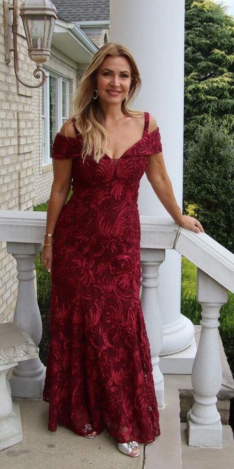 a woman in a red dress standing on a porch next to a white column and lamp post