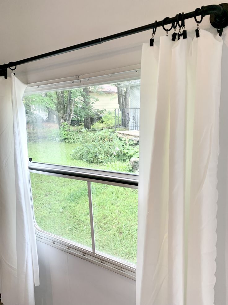 an open window with white curtains in front of it and trees outside the window sill