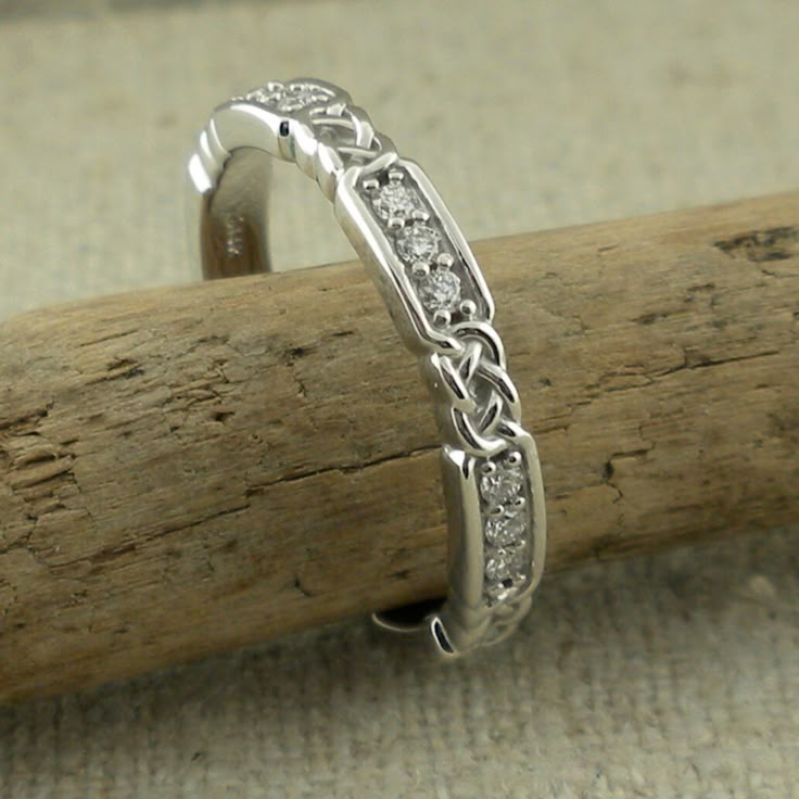 a white gold wedding band with diamonds on it sitting on top of a piece of wood