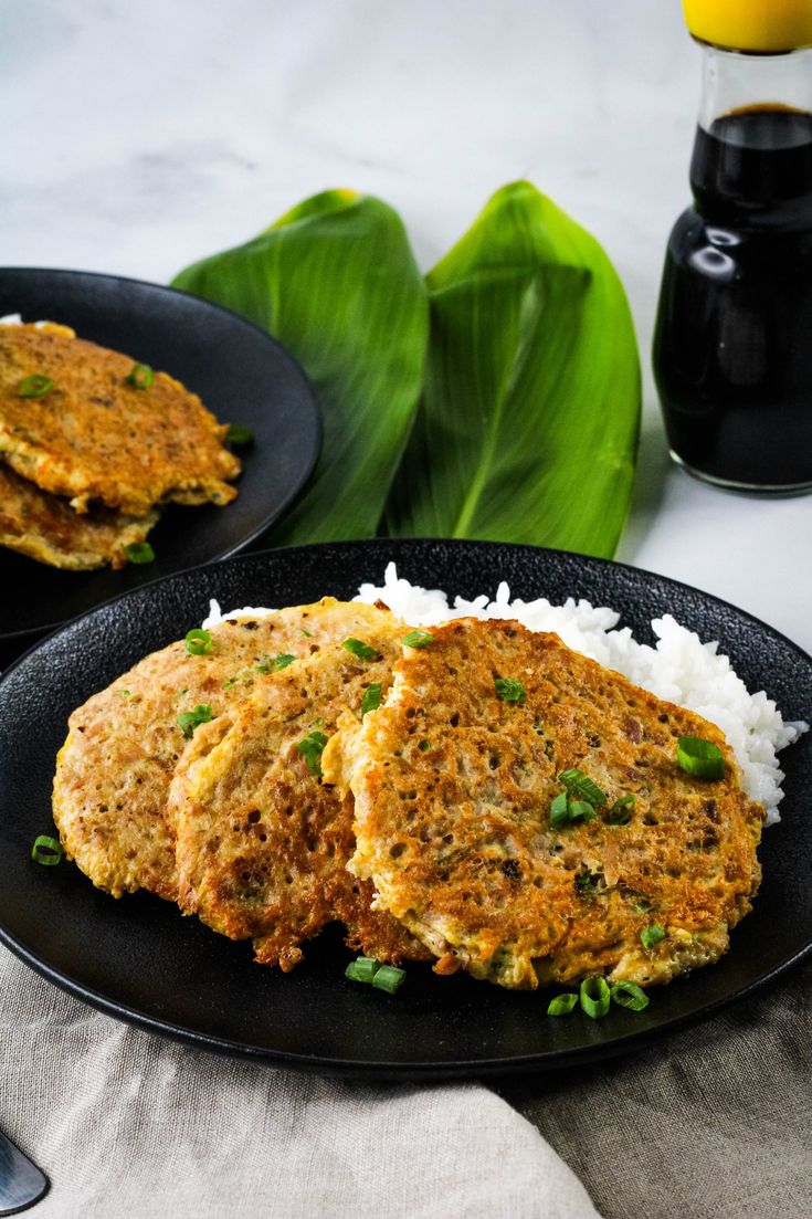 two patties with white rice and green onions on a black plate next to a glass of orange juice