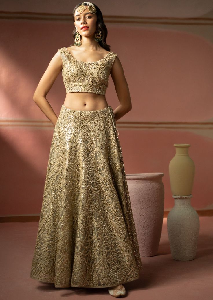 This lehenga set features heavy gold zari embroidery with mirrorwork. The short sleeves blouse has a plunging neckline. The lehenga set shows delicate tassels details. It is paired with a mirror embroidered organza dupatta with tassels on both sides. Traditional Palazzo Set With Gold Embroidery For Reception, Bollywood Palazzo Set With Gold Embroidery For Diwali, Festive Gold Lehenga With Mirror Work, Gold Lehenga With Mirror Work For Designer Wear, Gold Anarkali Choli With Mirror Work, Designer Gold Lehenga With Mirror Work, Gold Lehenga With Mirror Work For Reception, Gold Lehenga Saree With Mirror Work, Bollywood Style Gold Palazzo Set With Embroidery