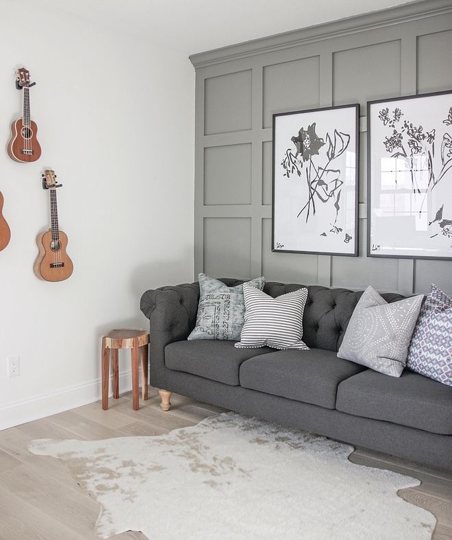 a living room with grey couches and guitars hanging on the wall behind them,