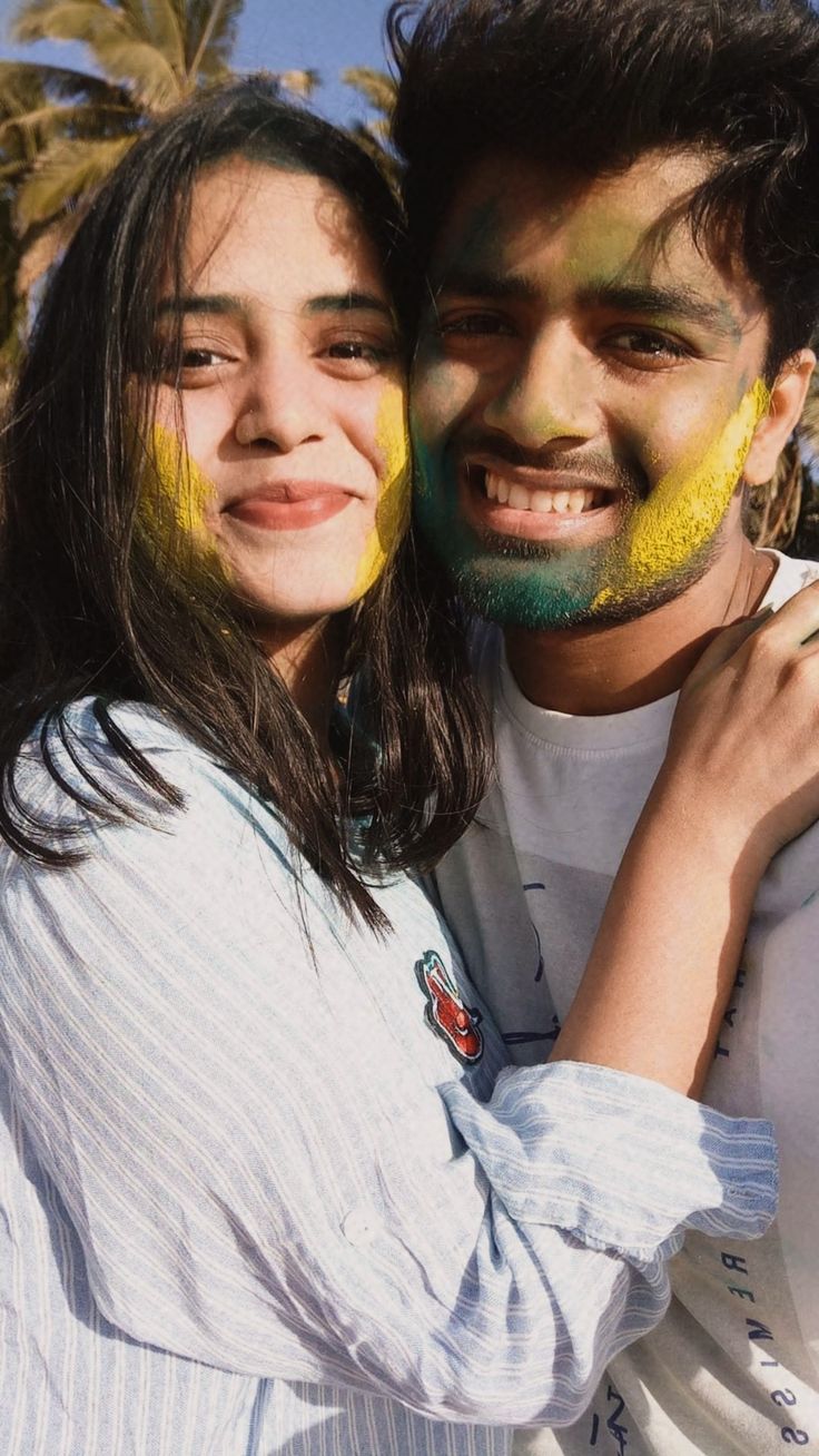 two people with painted faces pose for a photo in front of palm trees and blue sky