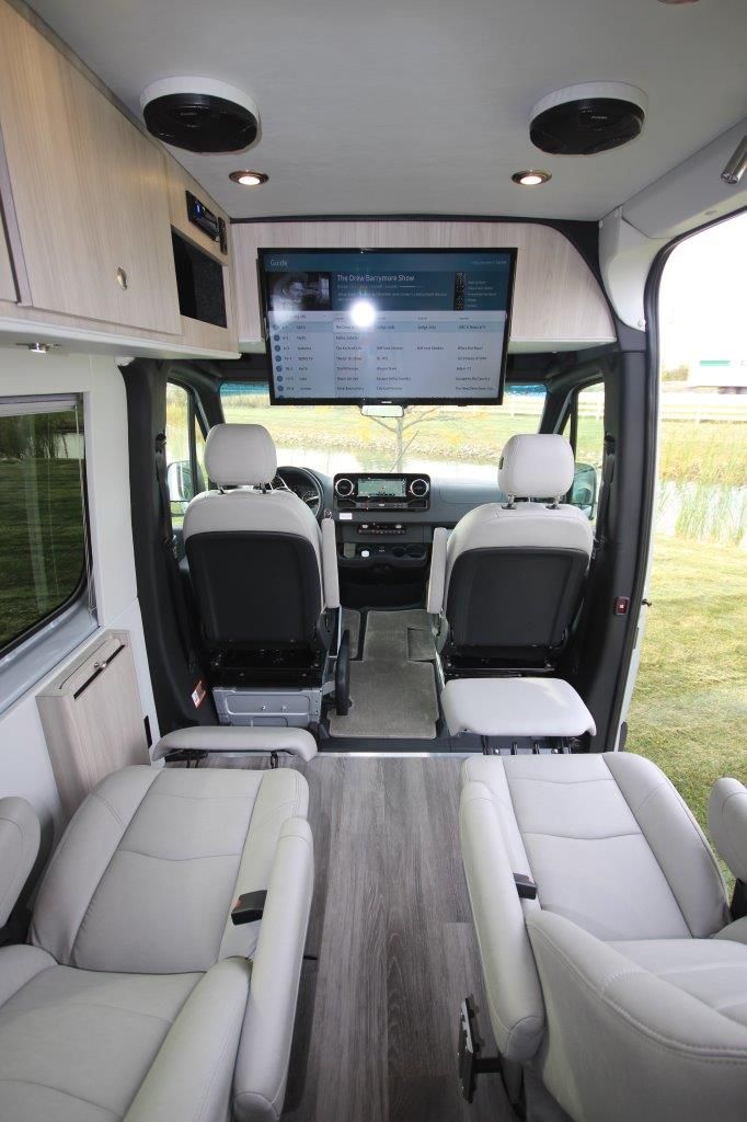 the interior of an rv with white leather seating and flat screen tv mounted to the wall