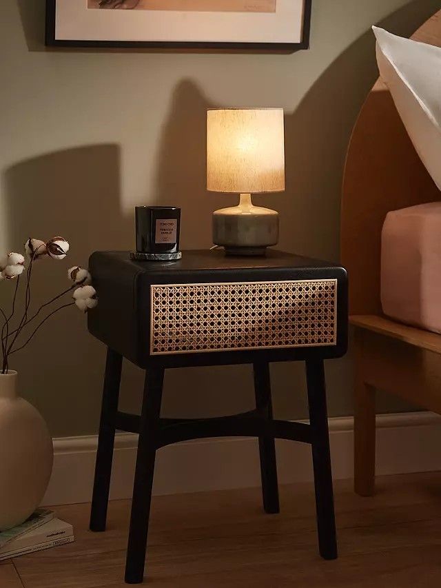 a night stand with a lamp on it in front of a painting and bedding