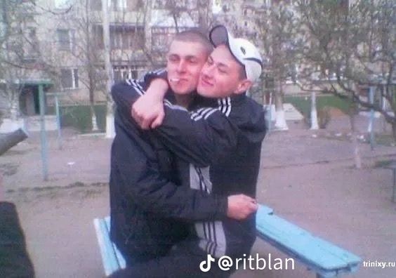 two young men hugging each other on a bench in front of some trees and buildings