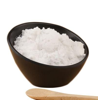 a wooden spoon next to a black bowl filled with white sugar on a white background