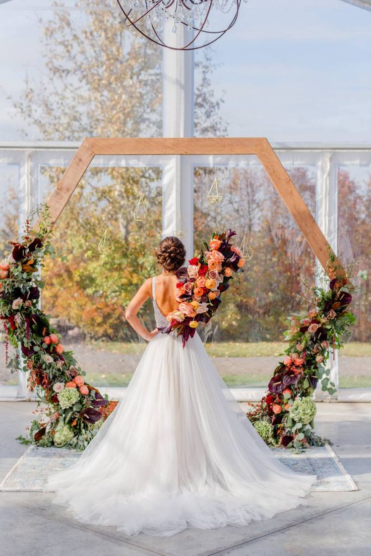 a woman wearing a wedding dress standing in front of an arch with flowers on it