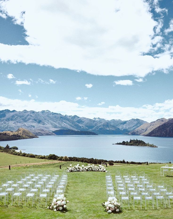 an outdoor ceremony set up with white chairs and flowers on the grass, overlooking a large body of water