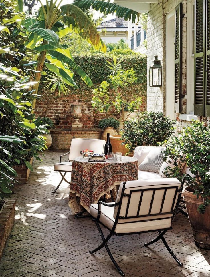 an outdoor patio with chairs, table and potted plants on the side of it