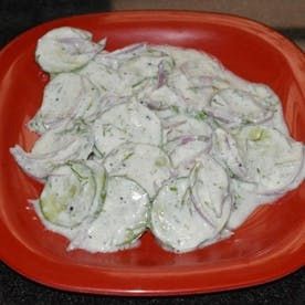 a red plate topped with cucumbers covered in white sauce on top of a black counter