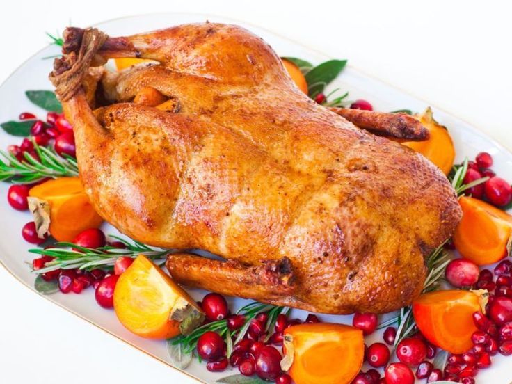 a roasted chicken on a platter with cranberries and oranges