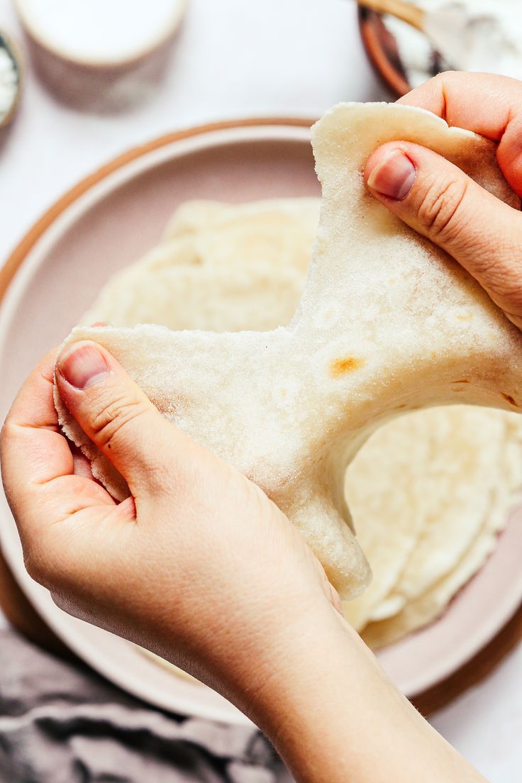 a person holding a piece of bread on top of a plate