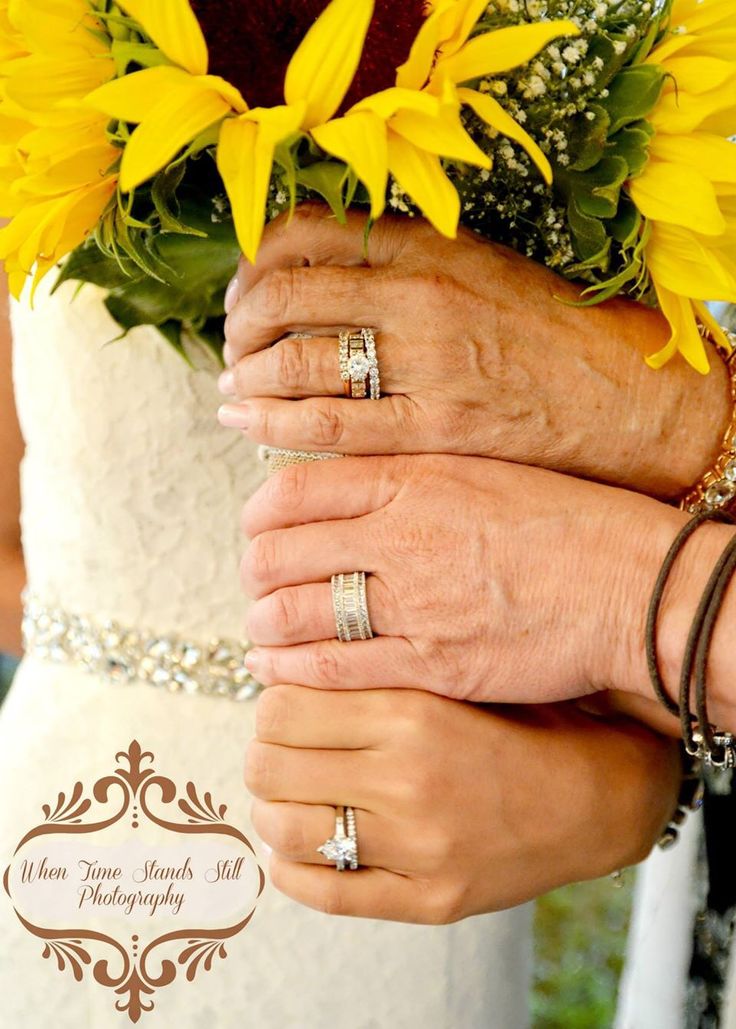 two brides holding hands with their wedding rings and sunflowers in the background