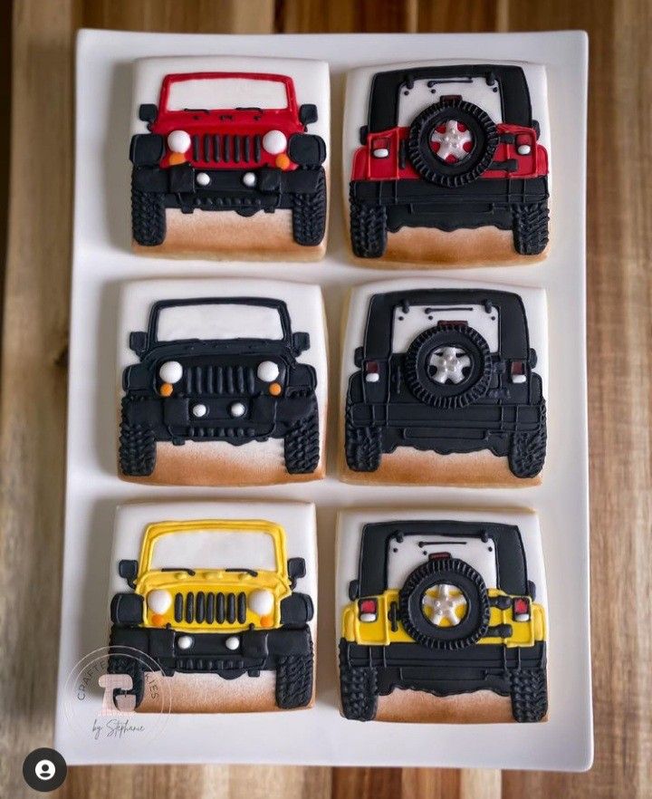 four decorated cookies in the shape of jeeps on a white tray with wood table