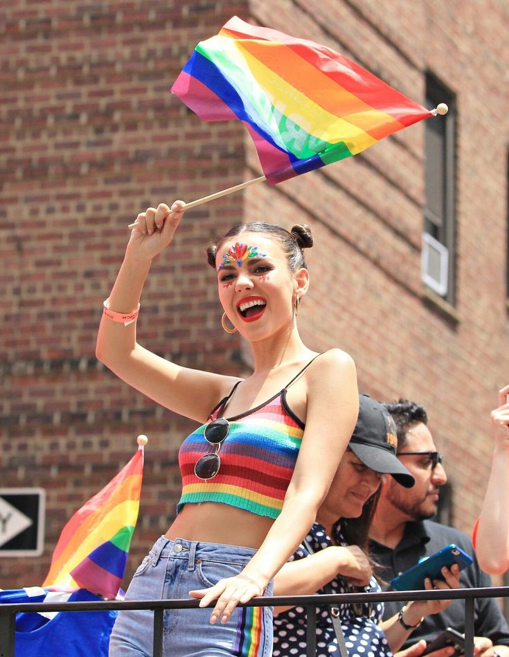 a woman holding a rainbow flag and waving it in the air while standing next to other people