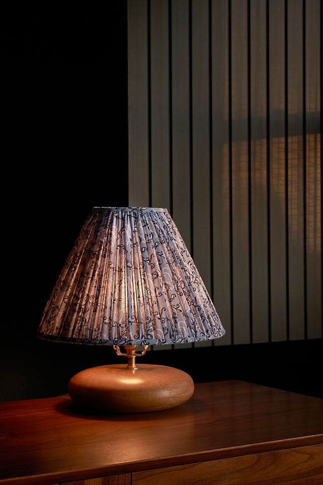 a lamp sitting on top of a wooden table next to a wall with vertical blinds