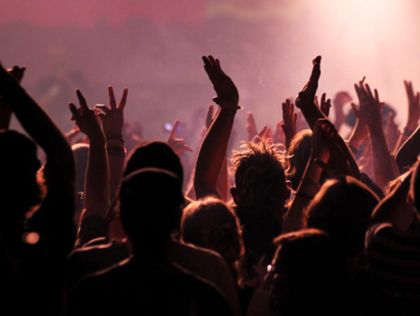 a crowd of people at a concert with their hands up in the air and lights on